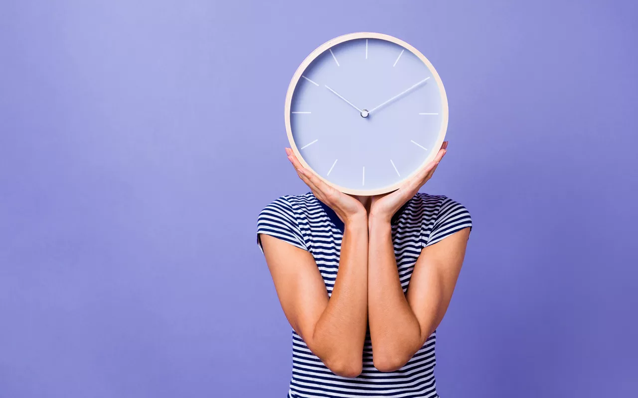 Eine Frau mit Kinderwunsch hält eine große Uhr. 