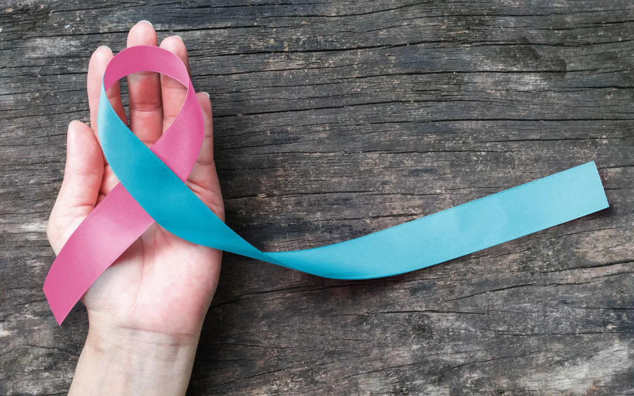 Eine blau-rosane Schleife liegt in einer Handfläche und steht symbolisch für die Sichtbarkeit und Unterstützung von Frauen, die eine Fehlgeburt hatten