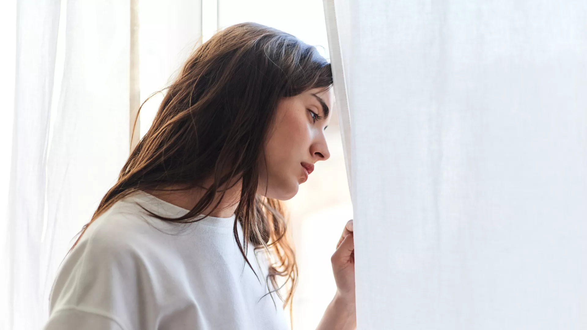 Eine Frau mit braunen Haaren schaut nachdenklich aus dem Fenster