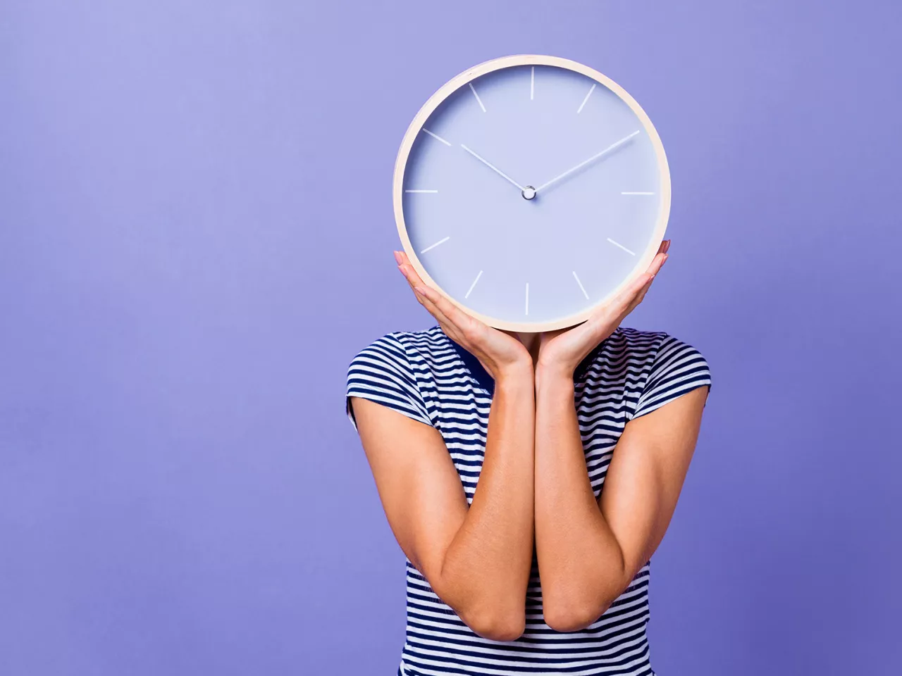 Eine Frau mit Kinderwunsch hält eine große Uhr. 