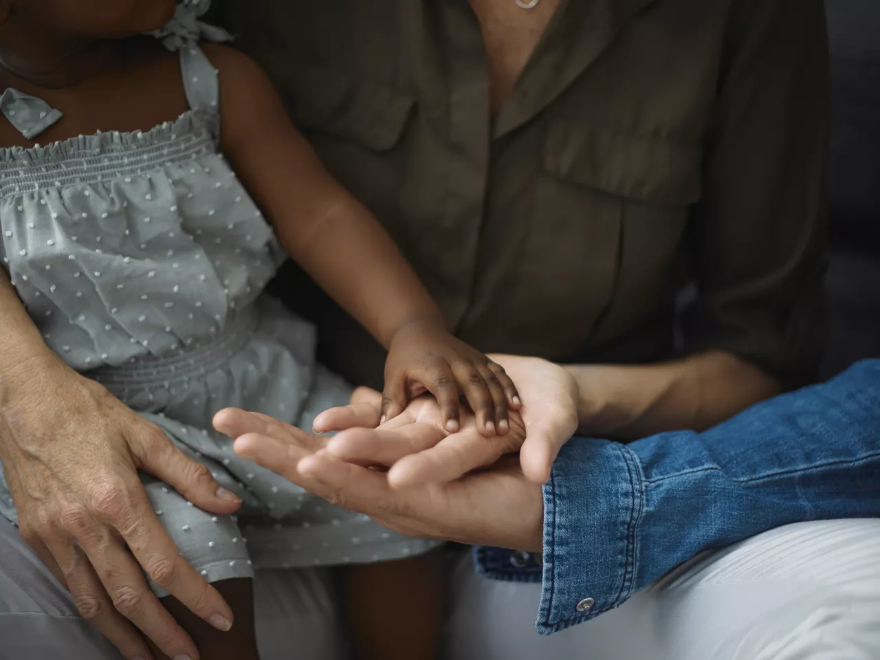 Es sind zwei Hände von erwachsenen sowie eine Hand von einem kleinen Kind zusehen, die gemeinsam Händchen halten.